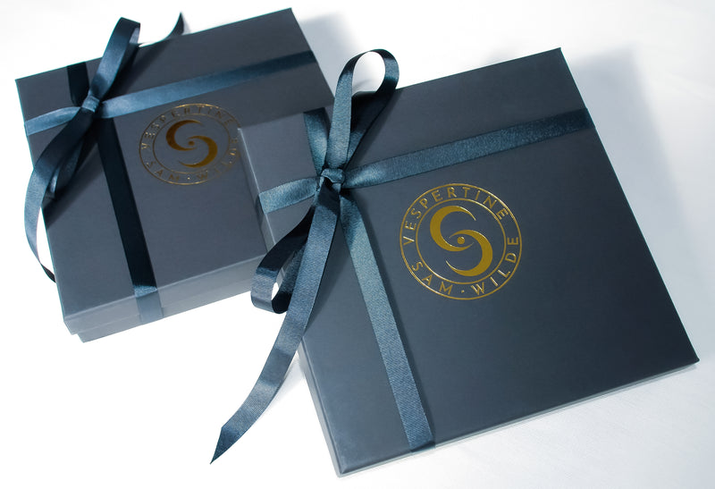Two chic matte black Vespertine scarf boxes featuring a gold embossed emblem.